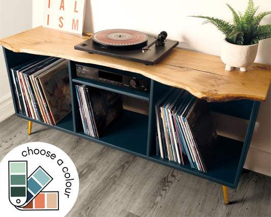 Front view of a vinyl record player cabinet featuring a live edge solid oak top, three compartments for vinyl storage, an amp shelf in the centre, and gold tapered metal legs.