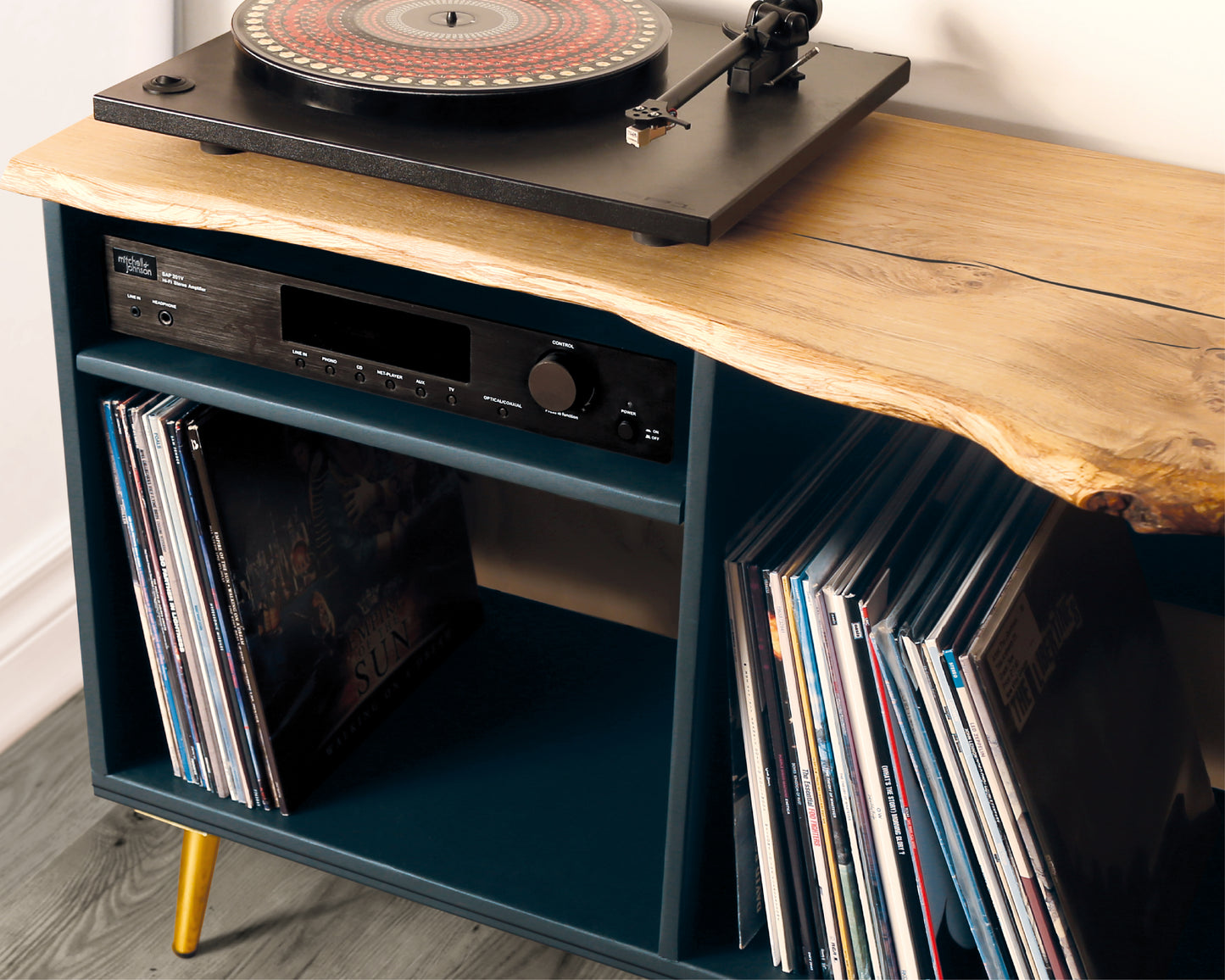 Close-up view of a vinyl record player cabinet showcasing the live edge solid oak top, smooth wood grain, and gold tapered metal legs, highlighting the craftsmanship and natural finish.